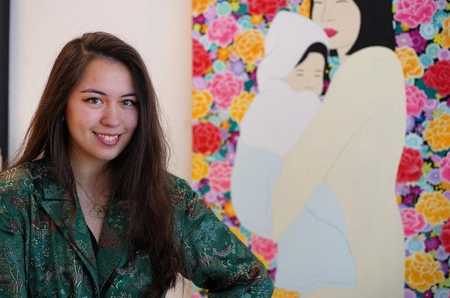 Artist Julia Chon in front of painting of mother and child on floral background