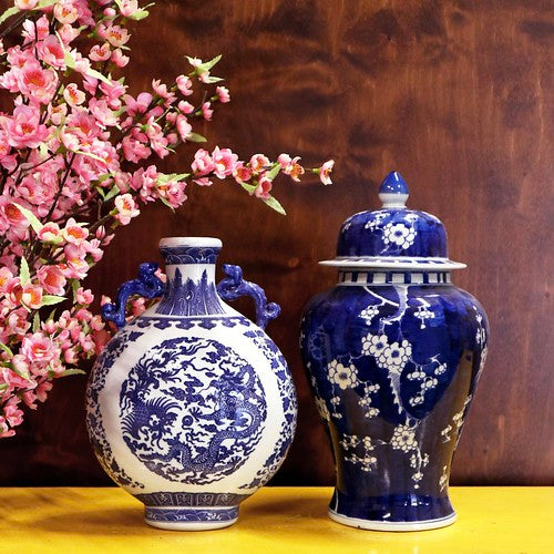 Two blue on white vases on yellow table with pink flowers