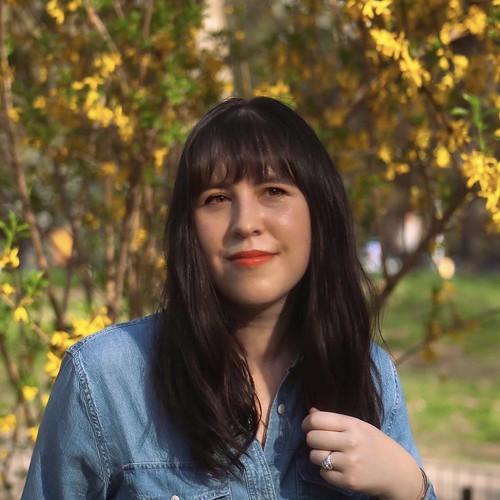 Woman with dark hair and blue shirt standing in front of tree