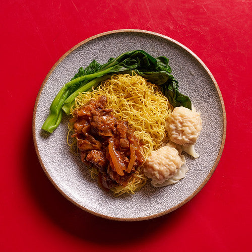 Dish of noodles with sauce, two wontons, and Chinese broccoli on red background