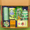 A box of tea lover items, including a canister of high quality green tea, matcha panda cookies, tin of jasmine tea, matcha candy, a mug, a handheld tea strainer, and ginger tea