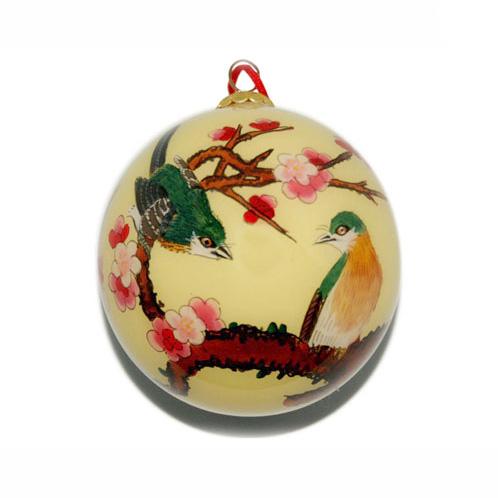 Holiday ornament with green and yellow birds on a branch of pink cherry blossoms